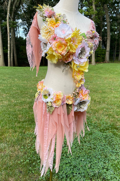 Person wearing a floral headpiece and pink feathered shoulders outdoors.